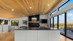 Una cocina moderna con una isla grande, un televisor montado en la pared y grandes ventanales con vistas al exterior.