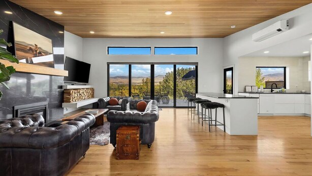 Una sala de estar moderna con un sofá de cuero, una mesa de centro y una chimenea. Hay una zona de cocina con una barra y un ventanal con vistas a un paisaje pintoresco.