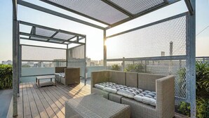 Eine Dachterrasse mit Korbmöbeln, einer Bank und Blick auf die Stadt.