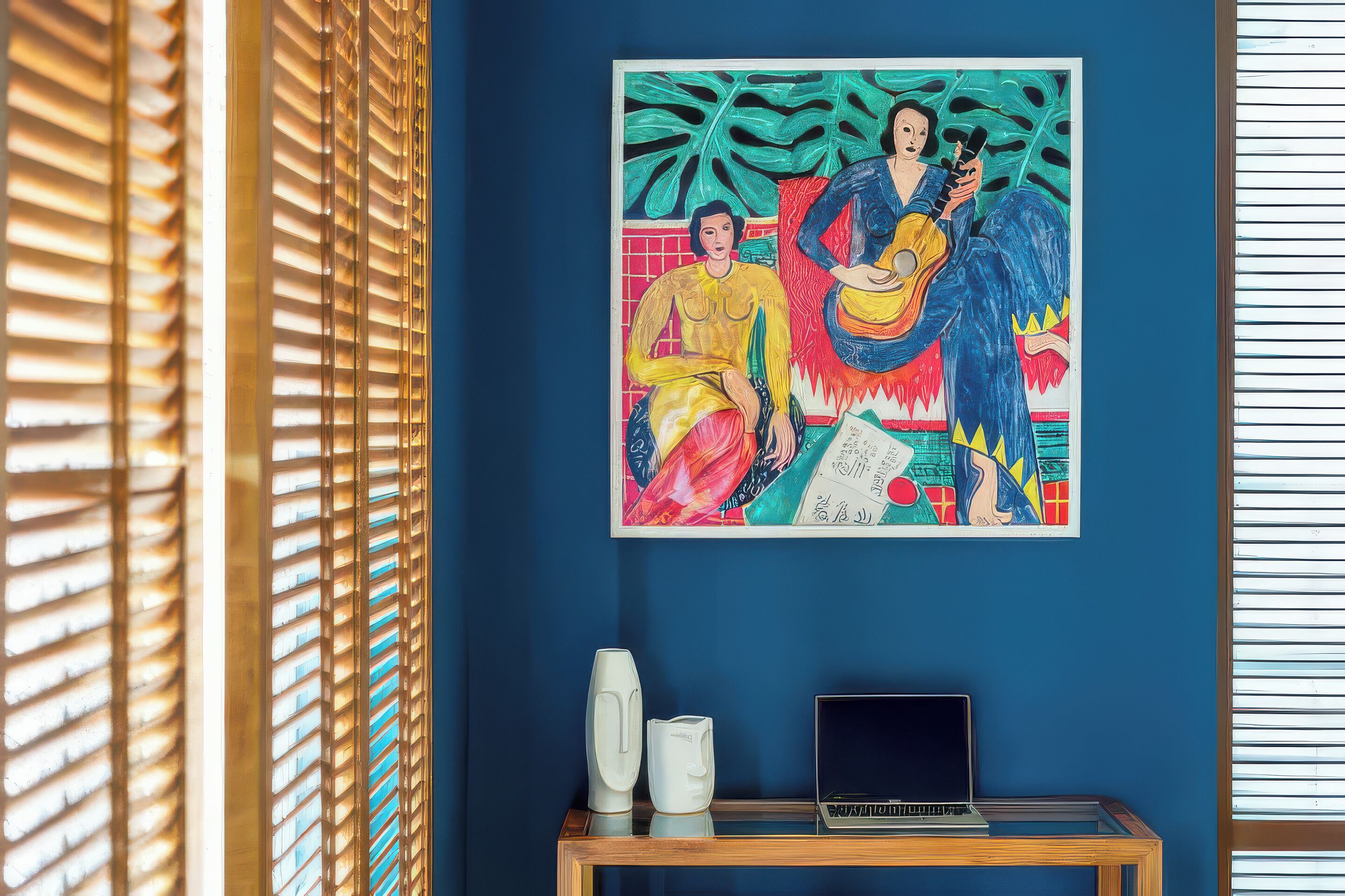 Una habitación con pared azul, un cuadro, una laptop y una cafetera sobre una mesa de madera.