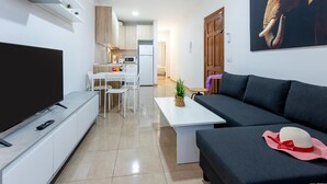 Ein modernes Wohnzimmer mit Flachbildfernseher, einer schwarzen Couch und einem Essbereich mit weißem Tisch und Stühlen.