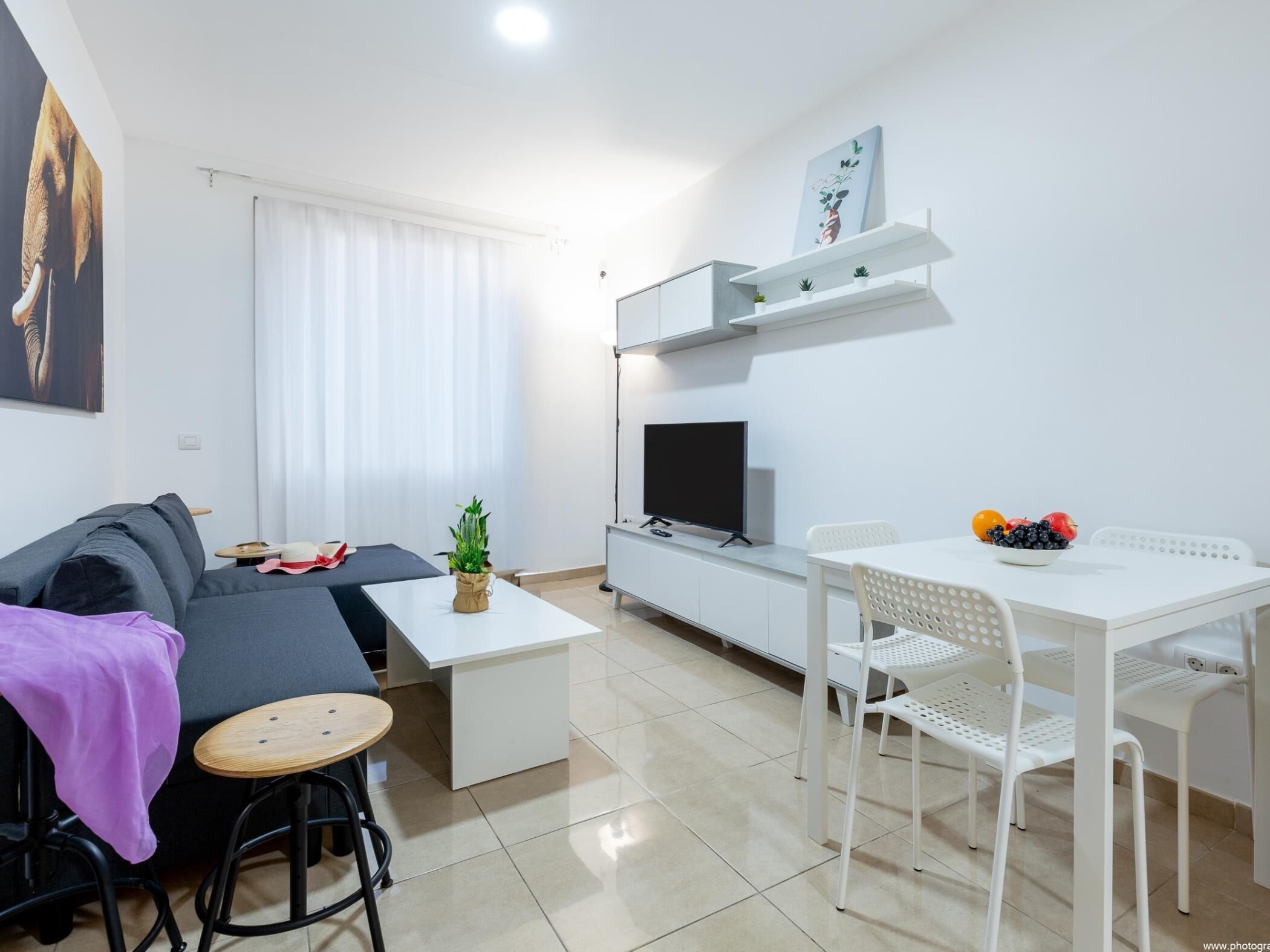En moderne stue med sofa, et lille bord, et fjernsyn og et spiseområde med stole.