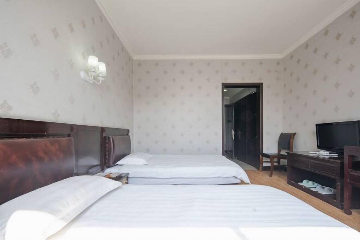 A hotel room with two beds, a television, a desk, and a shoe rack.