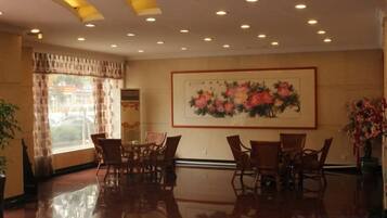 A hotel lobby with a dining area, a large floral painting on the wall, and a large window with curtains.