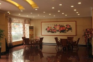 Un vestíbulo de hotel con zona de comedor, un cuadro grande con motivos florales en la pared y un amplio ventanal con cortinas.