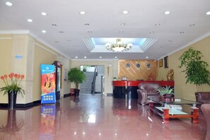 Un hall de hotel con mostrador de recepción, zona de estar y una escalera que conduce a los pisos superiores.