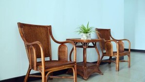 A room with two wicker chairs and a small table, a potted plant on the table, and a plain white wall. - Jinqiao Hotel (Anji)