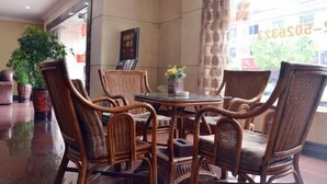 A dining area with wicker chairs around a glass table, a potted plant, and a framed menu on the wall. - Jinqiao Hotel (Anji)