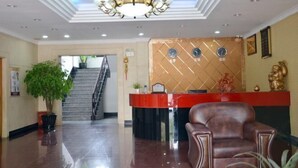 A hotel lobby with a reception desk, a staircase, and a large potted plant. - Jinqiao Hotel (Anji)