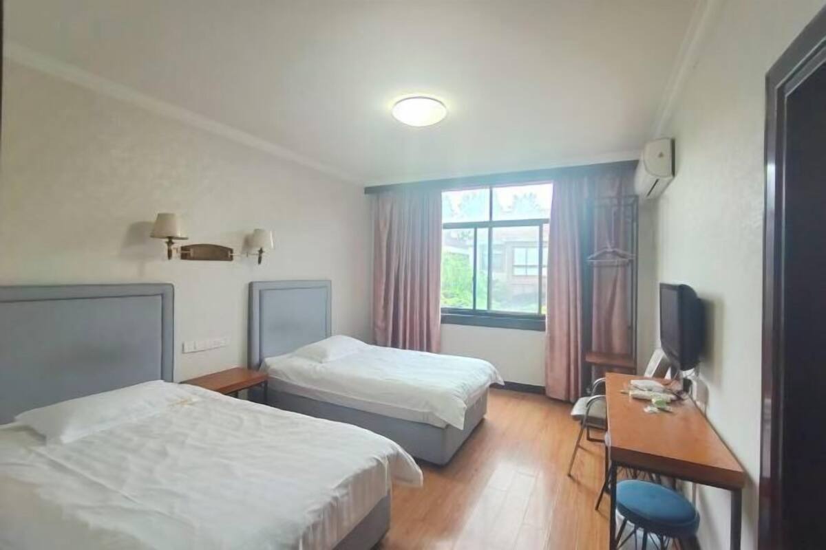 A hotel room with two beds, a desk with a chair, a television, and a window with curtains.