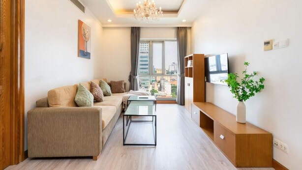 A modern living room with a sofa, coffee table, TV, and a view of the city through large windows.