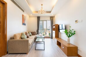 Ein modernes Wohnzimmer mit Sofa, Couchtisch, Fernseher und Blick auf die Stadt durch große Fenster.