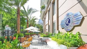 A rooftop patio with outdoor seating, palm trees, and a sign for the Ricons Group.