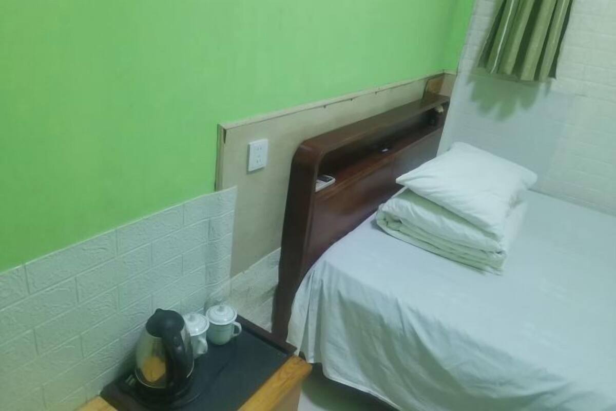 Una habitación pequeña con una cama, una mesita de noche con una tetera y una taza, y una pared verde.