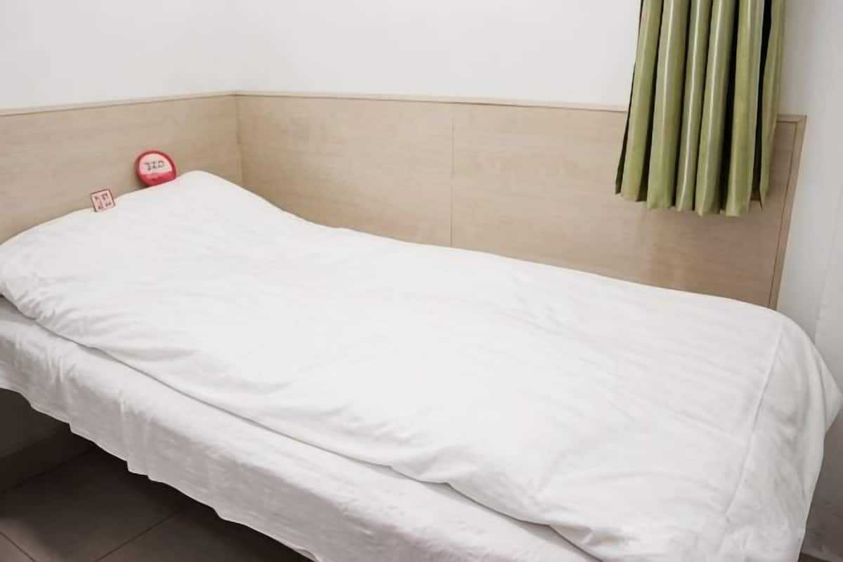 Una cama individual con colchón blanco y cabecera color beige en una habitación con suelo de baldosas.