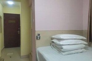 Una habitación de hotel con una cama, almohadas, una mesita de noche y una puerta.
