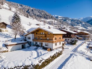 A multi-story wooden chalet with a snow-covered roof, surrounded by a snowy landscape and mountains. - Spacious apartment with beautiful mountain views (Zell am See)