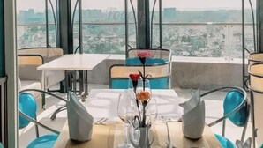 Een restaurant met een gedekte tafel voor twee, een bloevas en een stadszicht door een raam met patroon.