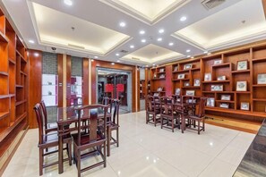 A hotel lobby with a central dining area, wooden bookshelves, and a tiled floor. - Yilong Hotel (Jingdezhen)