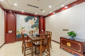 Un coin repas avec une table et des chaises en bois, un meuble décoratif agrémenté d’une plante, et un mur orné d’un tableau floral.