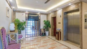 A hotel lobby with a reception desk, chairs, potted plants, an elevator, and a tiled floor. - Yilong Hotel (Jingdezhen)