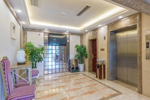 A hotel lobby with a reception desk, chairs, potted plants, an elevator, and a tiled floor. - Yilong Hotel (Jingdezhen)