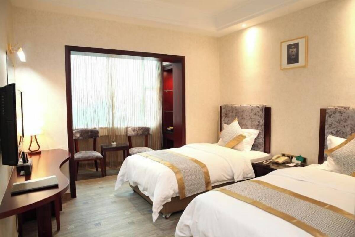 Habitación de hotel con dos camas, un escritorio, una silla y un televisor.