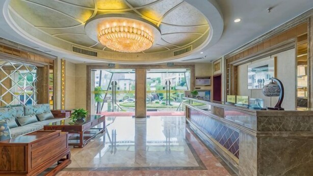 A hotel lobby with a grand chandelier, a reception desk, and a view of the outdoors. - Yilong Hotel (Jingdezhen)