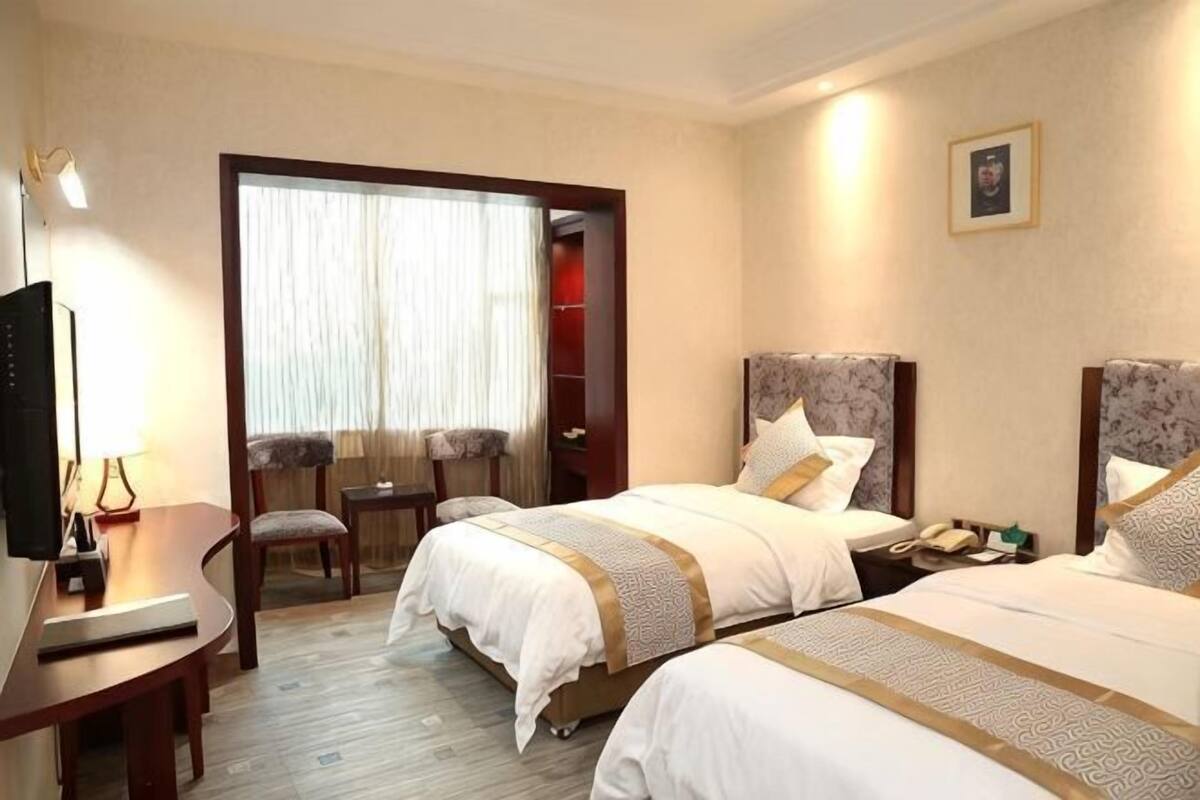 Habitación de hotel con dos camas, un escritorio, una silla, televisión y ventana con cortinas.