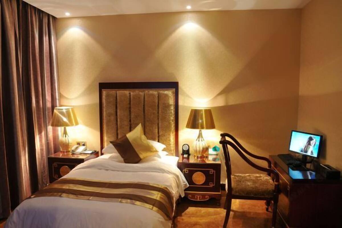 Una habitación de hotel con una cama grande, dos mesitas de noche con lámparas, un televisor y una silla.