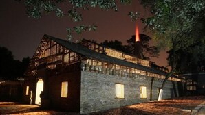 A traditional wooden building with a sloped roof, a stone wall, and a wooden deck. - Yilong Hotel (Jingdezhen)