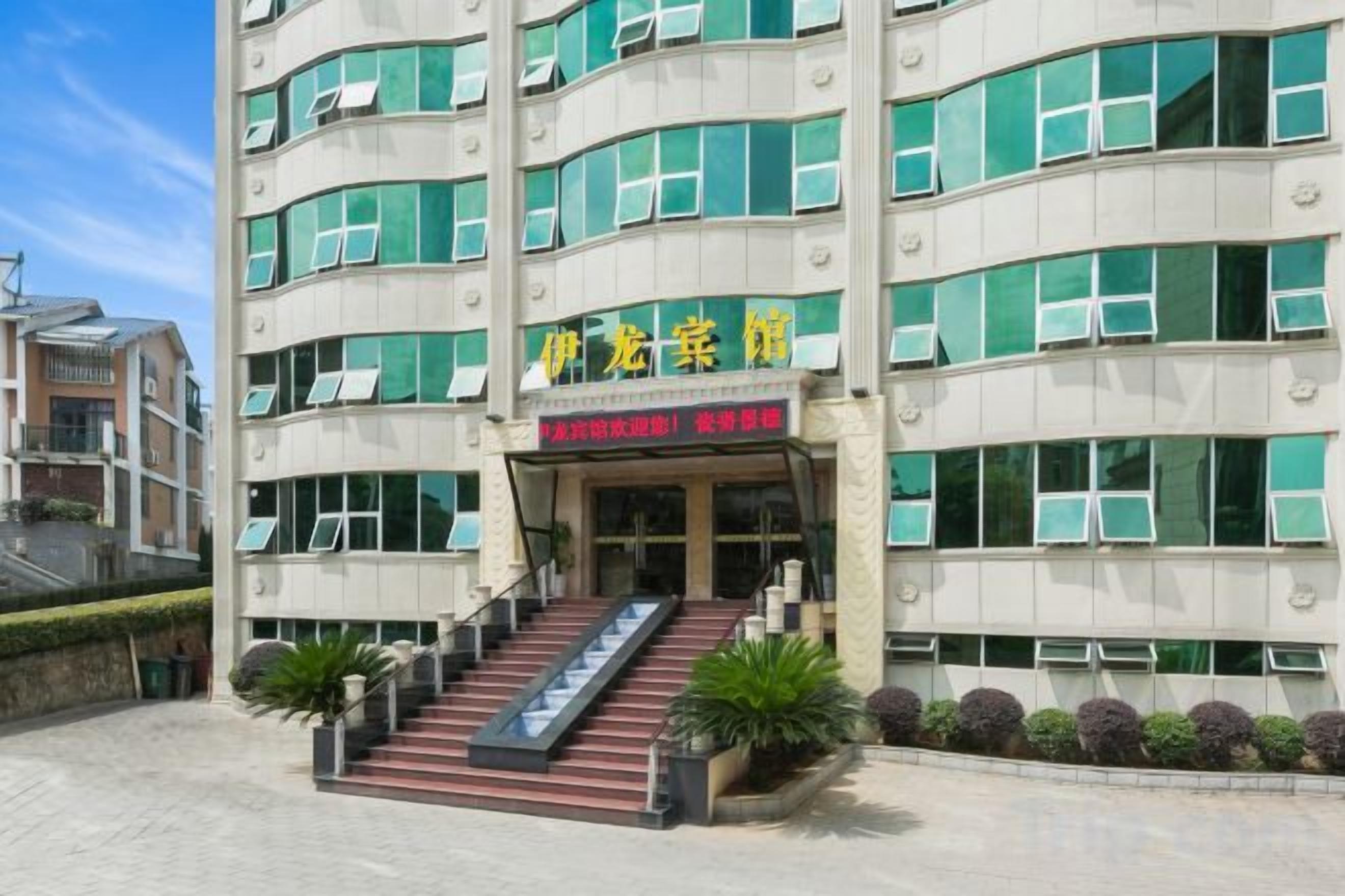 A multi-story hotel with a staircase leading to the entrance, surrounded by potted plants.