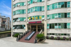 A multi-story hotel with a staircase leading to the entrance, surrounded by potted plants.