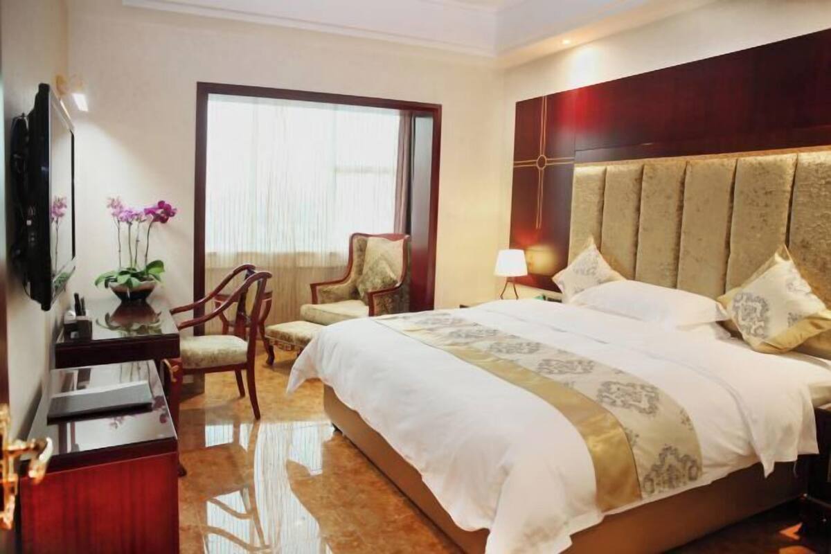Una habitación de hotel con cama, escritorio, silla, televisión y ventana con cortinas.