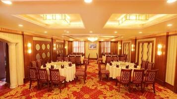 A banquet hall with round tables and chairs, a red carpet, and a chandelier.