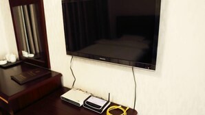 A hotel room with a flat-screen TV mounted on the wall, a wooden side table with a remote control, a power strip, and a yellow cable. - Kangding Dongsheng Business Hotel (Kangding)