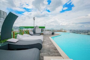 Piscina infinita en la azotea con sillas de descanso y vistas a la ciudad.