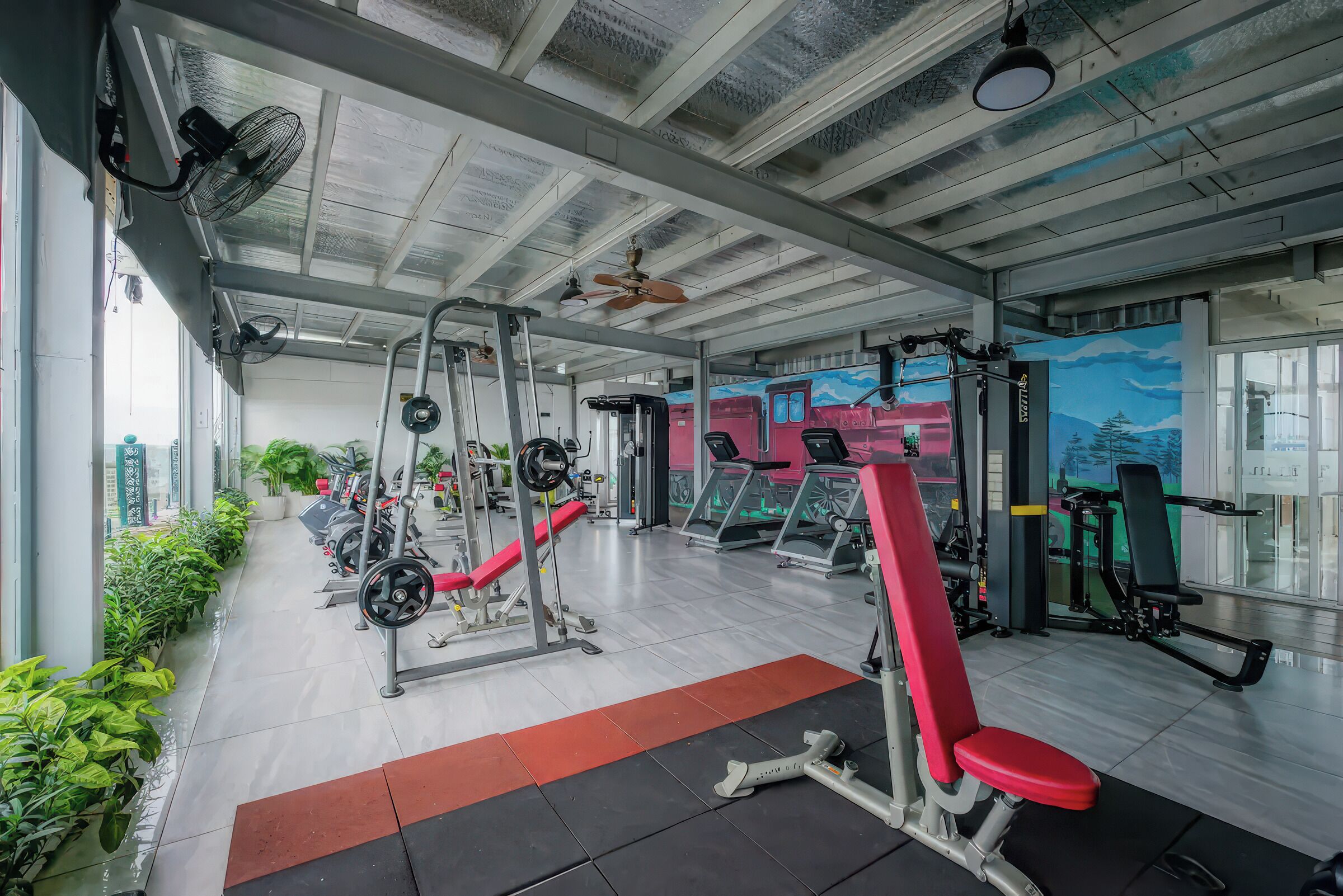 Ein Fitnessraum mit unterschiedlichen Trainingsgeräten, einem Deckenventilator und einem Wandgemälde.
