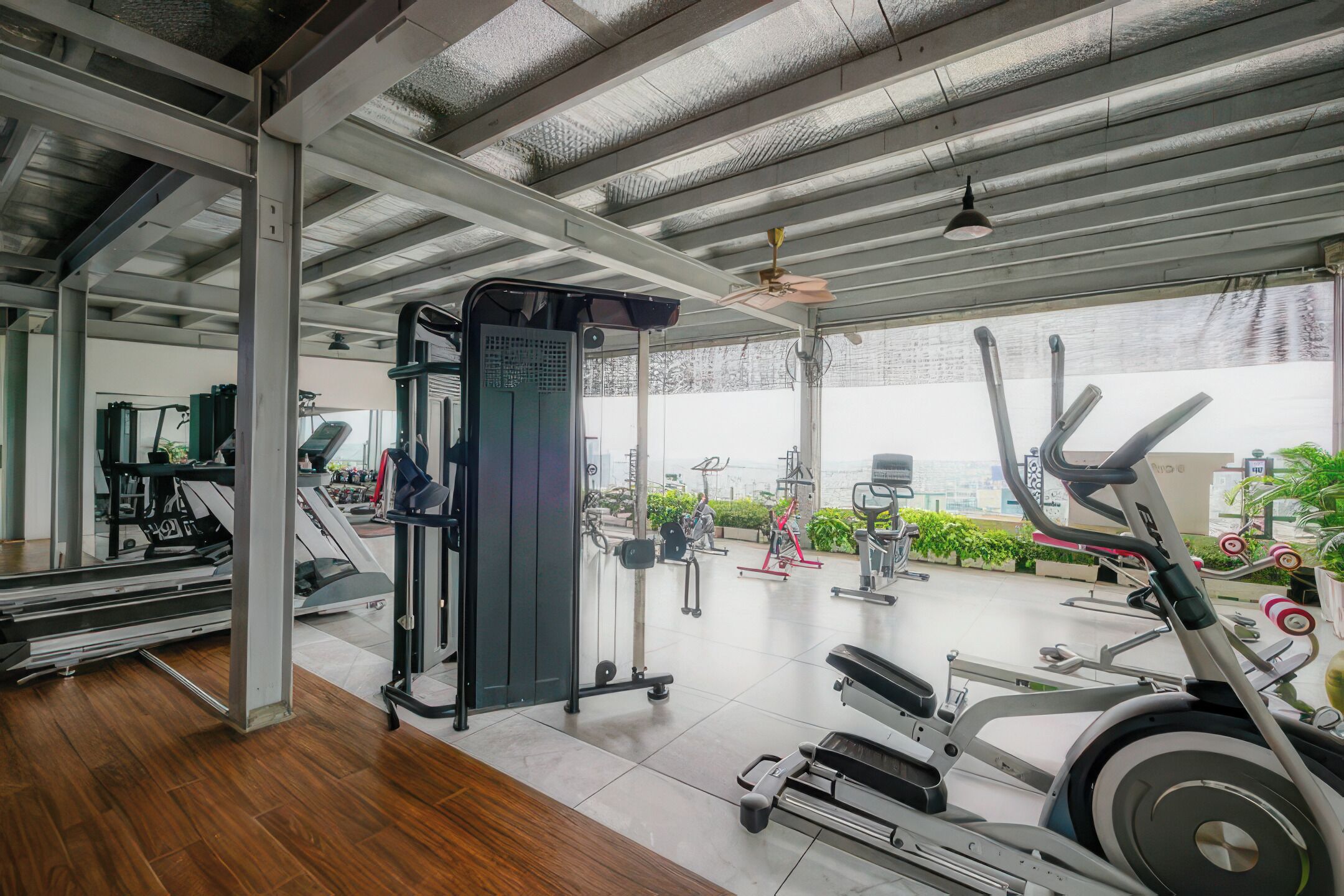 Un gimnasio con diferentes equipos de ejercicio, un ventilador de techo y vistas al verdor exterior.