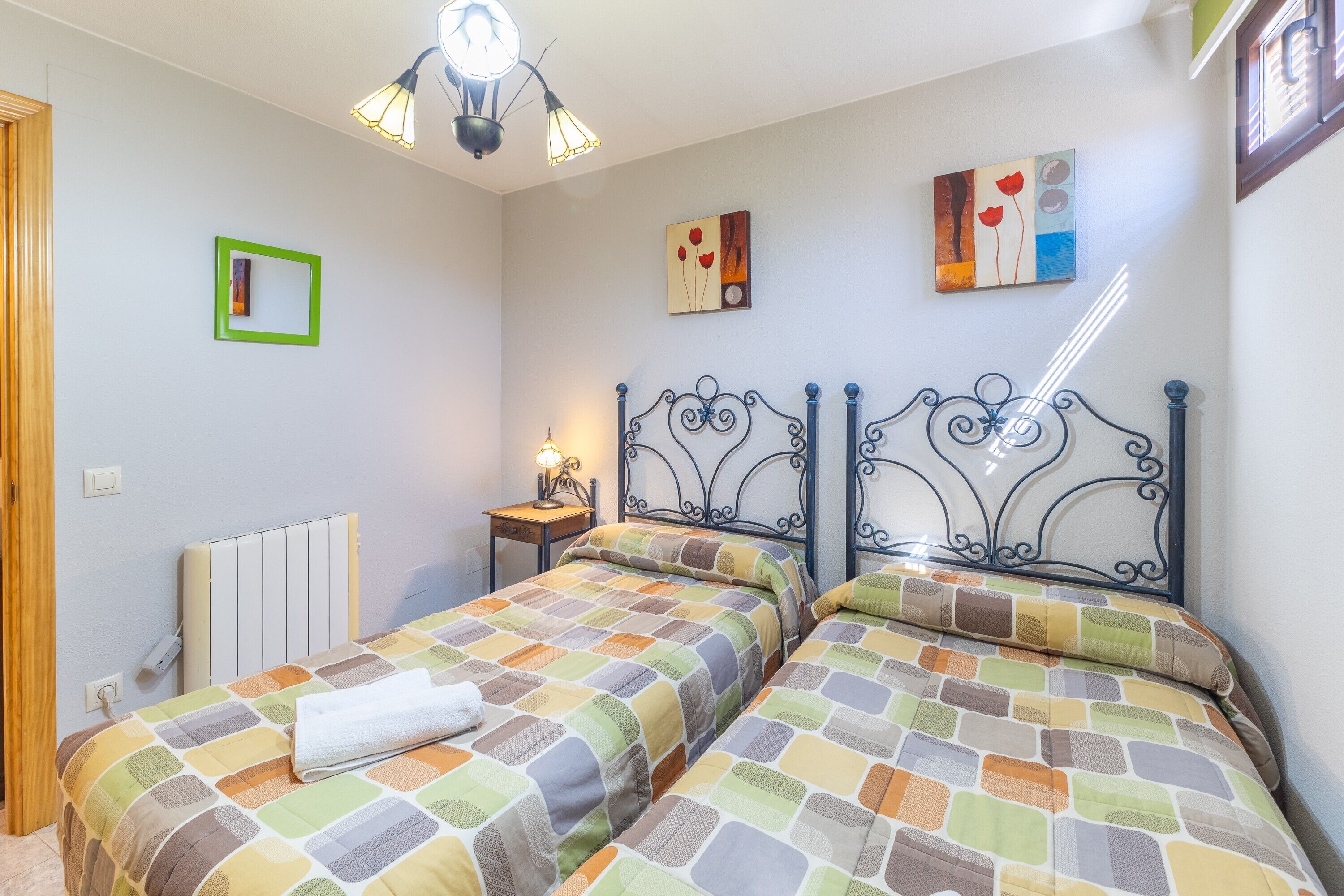 Une chambre avec deux lits, un radiateur, une table de chevet, une lampe et des œuvres d’art accrochées aux murs.
