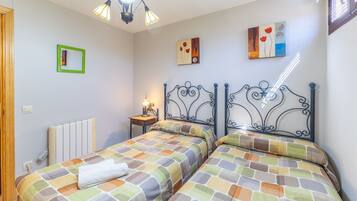 Une chambre avec deux lits, un radiateur, une table de chevet, une lampe et des œuvres d’art accrochées aux murs.