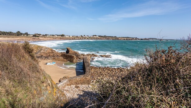 A coastal landscape with rocky terrain, a boat on the beach, and a clear sky.