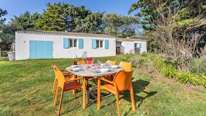 A white building with blue shutters, a round table with orange chairs, and a grassy yard.