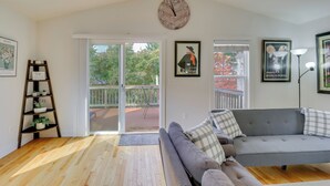 A living room with a grey sofa, a wooden floor, a clock, and a view of a balcony.