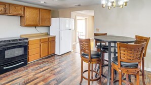 Una cocina con armarios de madera, un refrigerador blanco, un horno negro y una mesa de comedor con cuatro sillas de madera.