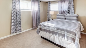 Un dormitorio con cama, cortinas, mesita de noche y lámpara.