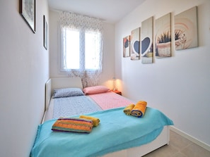 Un dormitorio con cama, almohadas, una lámpara de noche, una ventana con cortinas y decoración en la pared.