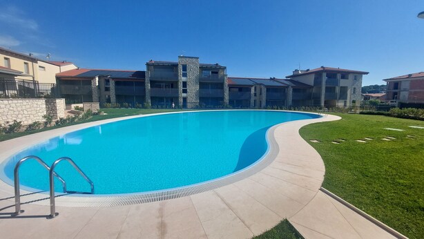 A swimming pool with a curved edge, surrounded by a paved walkway and a grassy area.