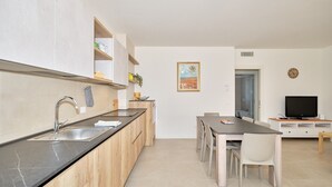 A modern kitchen with a black countertop, wooden cabinets, a stainless steel sink, and a dining area with a table and chairs.