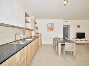 A modern kitchen with a black countertop, wooden cabinets, a stainless steel sink, and a dining area with a table and chairs. - Apartment 'New Casa Augusto' with Shared Pool, Wi-Fi and Air Conditioning (Lazise)